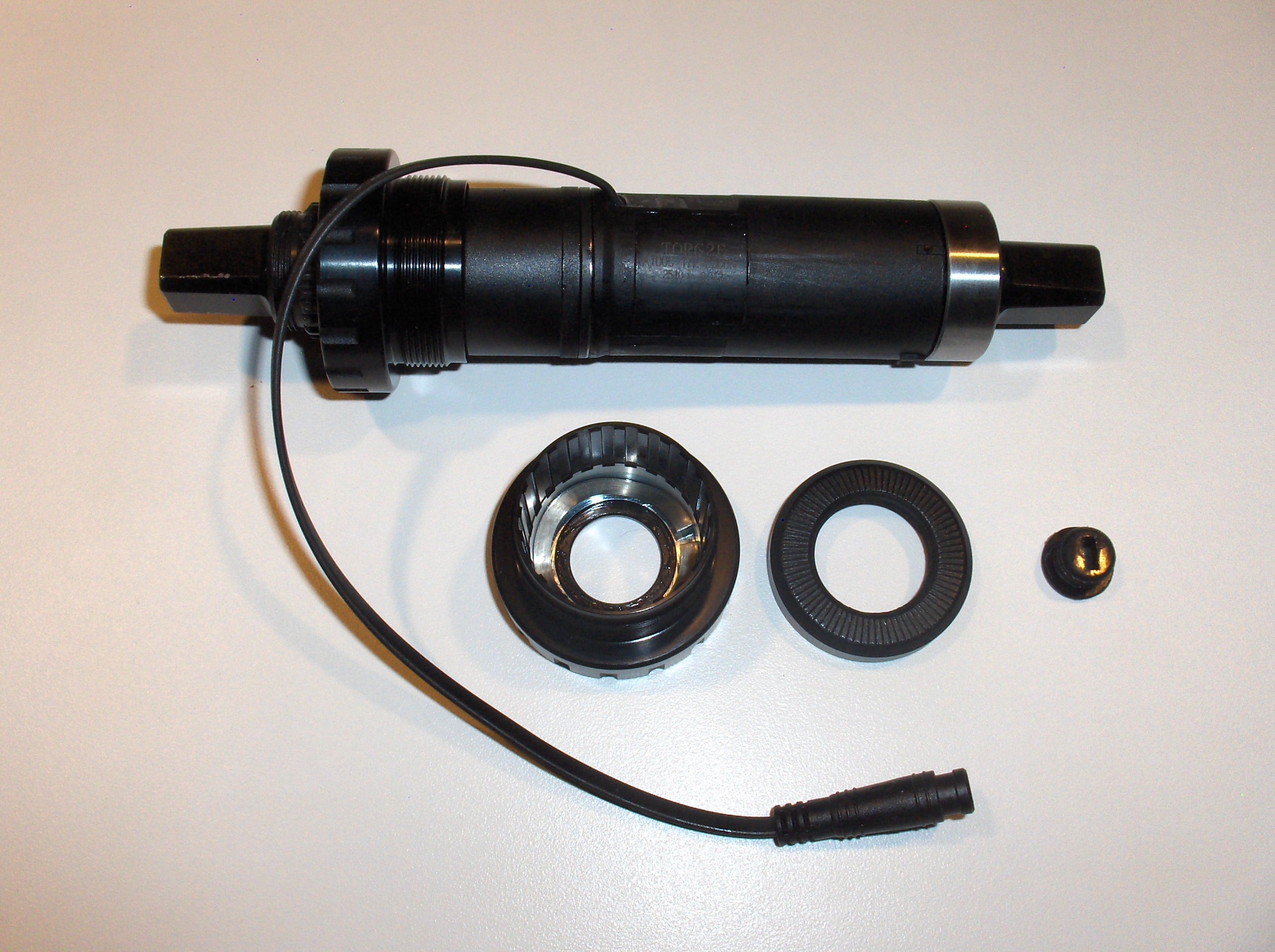 Black cylindrical component with attached cable and three additional black parts on a white background